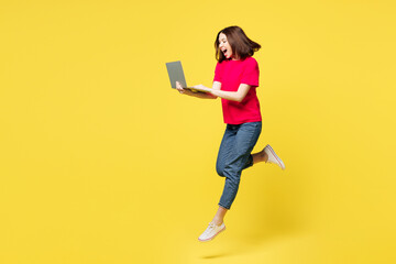 Wall Mural - Full body side view smart young IT woman in pink t-shirt casual clothes jump high hold use work on laptop pc computer run isolated on plain yellow orange background studio portrait Lifestyle concept