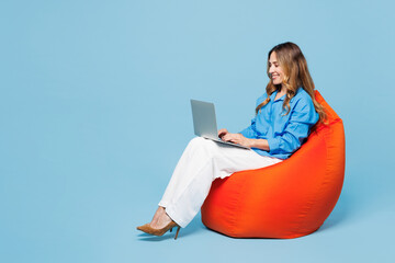 Full body young smart IT woman she wear shirt casual clothes sit in bag chair hold use work on laptop pc computer isolated on plain pastel light blue cyan background studio portrait Lifestyle concept