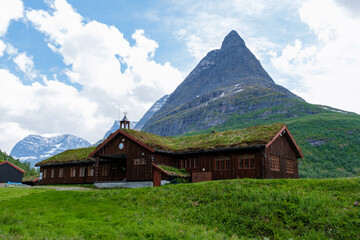 Wall Mural - In Norway, a rustic wooden cabin with a grassy roof is nestled among lush green mountains, creating a serene and beautiful landscape. Innerdalen Norway's most beautiful mountain valley