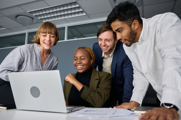 Wall Mural - Four happy young adults in businesswear working on laptop at desk in office