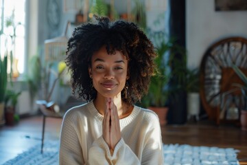 Poster - Portrait of a tender afro-american woman in her 20s joining palms in a gesture of gratitude isolated on scandinavian-style interior background