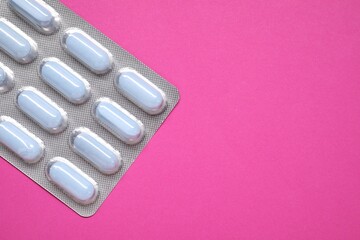 Wall Mural - Pills in blister on pink background, top view. Space for text