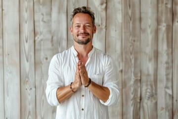 Poster - Portrait of a joyful caucasian man in his 40s joining palms in a gesture of gratitude over light wood minimalistic setup
