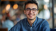 © Jack - Close-up portrait of a young smiling man in glasses and a blue shirt sitting and working in the office and looking confidently at the camera