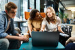 © LIGHTFIELD STUDIOS - Multicultural colleagues gather around a laptop in a hotel lobby during a corporate trip, discussing business strategies.