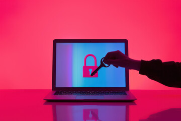 Poster - hand is holding a key unlocking a padlock on a laptop screen with a cool pink and blue background su