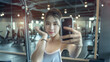 © tiagozr - Young woman taking a gym selfie in front of mirror.