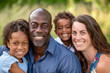 © PixelGallery - Portrait of a diverse family, parents and kids smiling and hugging in a green park