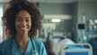 © Galib - A Black woman nurse in a hospital room smiles at the camera.