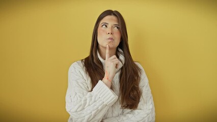 Canvas Print - Pensive young hispanic woman with a thoughtful expression, fingers on chin, lost in her thoughts, standing alone, concentrated in doubt, wearing a sweater over a vibrant yellow background.