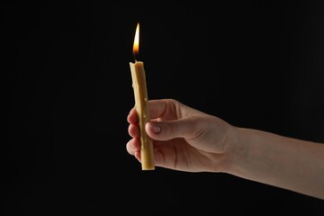 Wall Mural - Woman holding burning church candle on black background, closeup