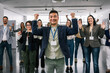 © Mediteraneo - Portrait of young Asian CEO standing in front of his multiracial colleagues with their hands in the air, celebrating their success.