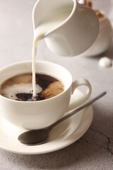 Poster - Pouring milk into cup with coffee on light grey textured table, closeup