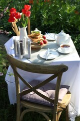 Canvas Print - Beautiful bouquet of tulips and freshly baked waffles on table served for tea drinking in garden