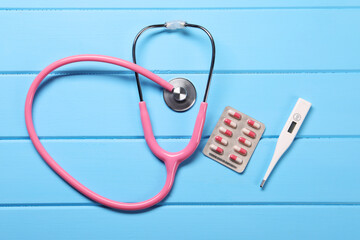 Wall Mural - Stethoscope, thermometer and pills on light blue wooden background, flat lay. Medical treatment