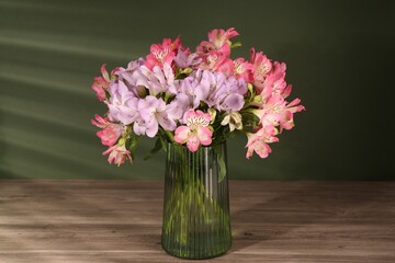 Canvas Print - Beautiful alstroemeria flowers in vase on wooden table against green background