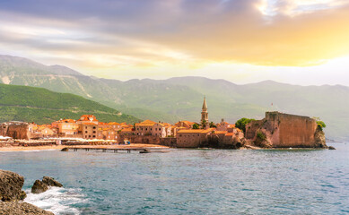 summer season landscape of old town on sea shore with antique wall and tower, blue water vawes and beautiful mountains and cloudy sky on background