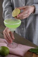 Wall Mural - Woman squeezing lime juice into glass with delicious Margarita cocktail at wooden table, closeup
