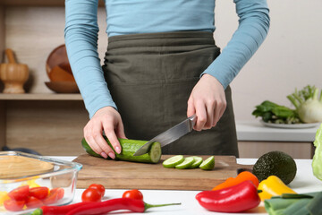 Wall Mural - Healthy food. Woman cutting cucumber at white table in kitchen, closeup