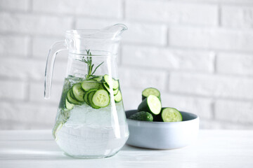 Sticker - Refreshing cucumber water with rosemary in jug and vegetables on white table against brick wall
