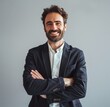 © pham - A man in a black blazer with his arms crossed smiles confidently at the camera. He is standing in front of a plain grey background