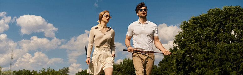 A young couple in elegant clothing walks across a luxurious golf course, enjoying the refined atmosphere.