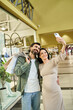 © LIGHTFIELD STUDIOS - A pregnant woman and man happily pose for a selfie while shopping together in a bustling mall.