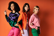 © LIGHTFIELD STUDIOS - Young multicultural women in stylish vibrant clothes stand together on an orange background.