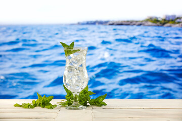 Wall Mural - Glass with water on the table with blue ocean and blurred city coastline in distance in summer