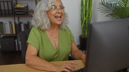 Poster - Success! middle age woman employee with grey hair happily pointing up one finger to show she has a great idea in the office workspace