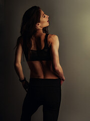 Wall Mural - Sporty sexy beautiful slim woman with long hair posing in black sport bra standing on wall background with empty copy space. Healthy lifestyle vintage