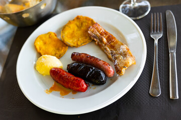 Wall Mural - Delicious traditional Spanish mixed grill plate featuring sausages, grilled pork slice, and fried eggplants, served with spicy aioli and glass of red wine