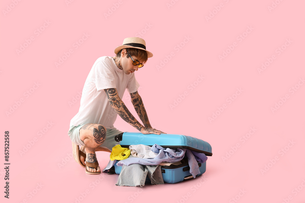 Young man trying to close suitcase on pink background