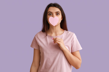 Wall Mural - Beautiful young girl with pink paper heart on purple background. Valentine's Day celebration