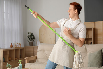 Wall Mural - Young man having fun with floor mop in living room