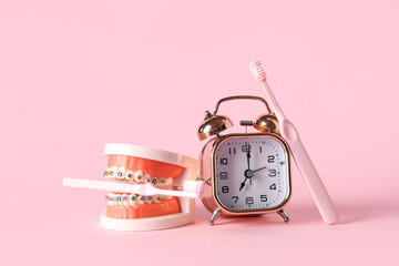 Alarm clock, model of jaw with dental braces and toothbrushes on pink background