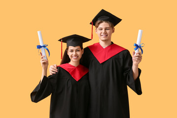 Wall Mural - Happy graduate couple with diplomas on yellow background