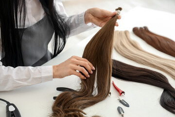 Female hairdresser with strand of hair at table in beauty salon, closeup