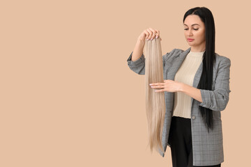 Wall Mural - Female hairdresser with strand of blonde hair on beige background