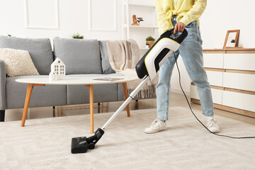 Canvas Print - Young woman cleaning carpet with cordless stick vacuum cleaner in living room