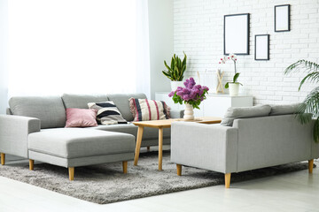 Canvas Print - Stylish interior of living room with bouquet of lilacs branches on coffee table near grey sofas