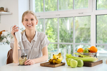Wall Mural - Happy young woman with blender and ingredients making healthy smoothie in kitchen