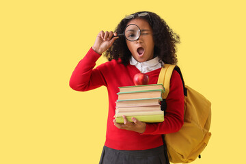 Canvas Print - Shocked little African-American schoolgirl with magnifier and books on yellow background