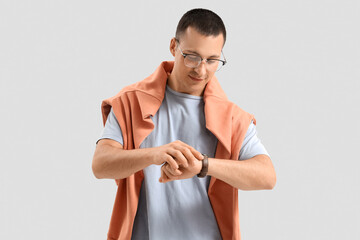 Wall Mural - Handsome young man in stylish outfit looking at wristwatch on grey background