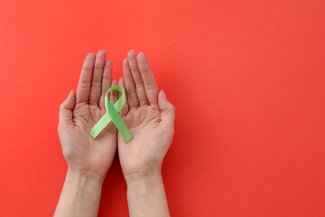 Wall Mural - Woman with light green awareness ribbon on red background, top view. Space for text