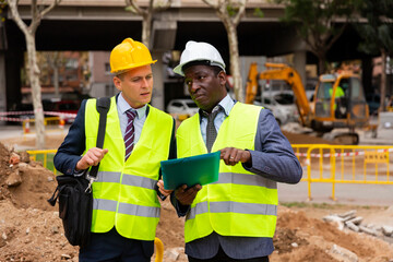 African-american and European men engineers discussing project documentation of road repairing works.