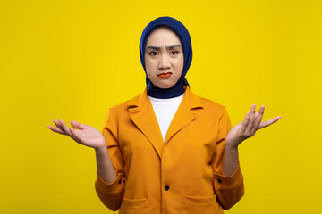 Wall Mural - Confused young Asian woman raising hands and shrugging shoulders, making I don't know gesture isolated on yellow background