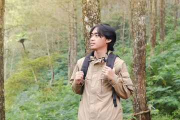 Portrait of excited Asian hiker man trekking and hiking in forest nature, wearing backpack and jacket for outdoor camping. Mountain travel concept