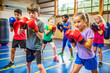 © thanakrit - Group of children in a gym practicing boxing with gloves, focused and determined. Physical activity, teamwork, and self-discipline.