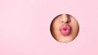 © Prostock-studio - A close-up view of a woman lips protruding out of a hole against a vibrant pink background. The lips appear to be puckered or in a kissing gesture.